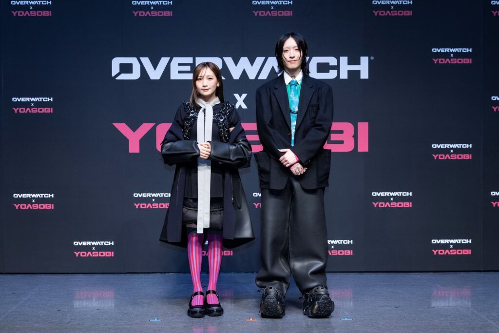 Parceria introduz visuais temáticos para Kiriko, Genji e Hanzo, além do lançamento de um álbum especial e contos narrativos focado no passado dos heróis.

A desenvolvedora de Overwatch revelou, durante um evento especial realizado em Tóquio, uma nova colaboração oficial com a dupla de J-Pop YOASOBI. A partir do dia 30 de junho, os jogadores poderão participar de um evento in-game focado na combinação entre combate, música e estilo. A parceria introduzirá itens cosméticos e recompensas que permitirão aos jogadores ouvir as faixas da dupla dentro do próprio jogo.

Seguindo a estrutura da técnica jornalística da pirâmide invertida, o foco principal da atualização fica por conta das recompensas visuais. Os desenvolvedores confirmaram que a colaboração trará skins (visuais) inéditas voltadas especificamente para o núcleo de heróis japoneses do título: Kiriko, Genji e Hanzo.

Narrativa expandida a partir de hoje
A integração entre o universo do jogo e a dupla musical vai além dos itens virtuais e já teve início. Para estabelecer o contexto do evento, um novo conto oficial foi disponibilizado aos jogadores hoje. A narrativa acompanha o herói ciborgue Genji em uma viagem a Tóquio, onde ele revisita o passado e relembra momentos de sua infância ao lado de seu irmão, Hanzo, e de Kiriko.

Edição especial do álbum "THE BOOK"
A colaboração se estenderá também ao mercado fonográfico, atuando como um prelúdio para a chegada do conteúdo aos servidores do jogo. No dia 26 de junho, os fãs terão acesso ao último capítulo da série de álbuns “THE BOOK”, produzida pela YOASOBI.

Esta edição especial será totalmente temática de Overwatch e trará material inédito. O destaque do lançamento musical é a faixa confirmada intitulada “Orion”, que teve sua composição inspirada diretamente no novo conto focado na história e infância de Genji.