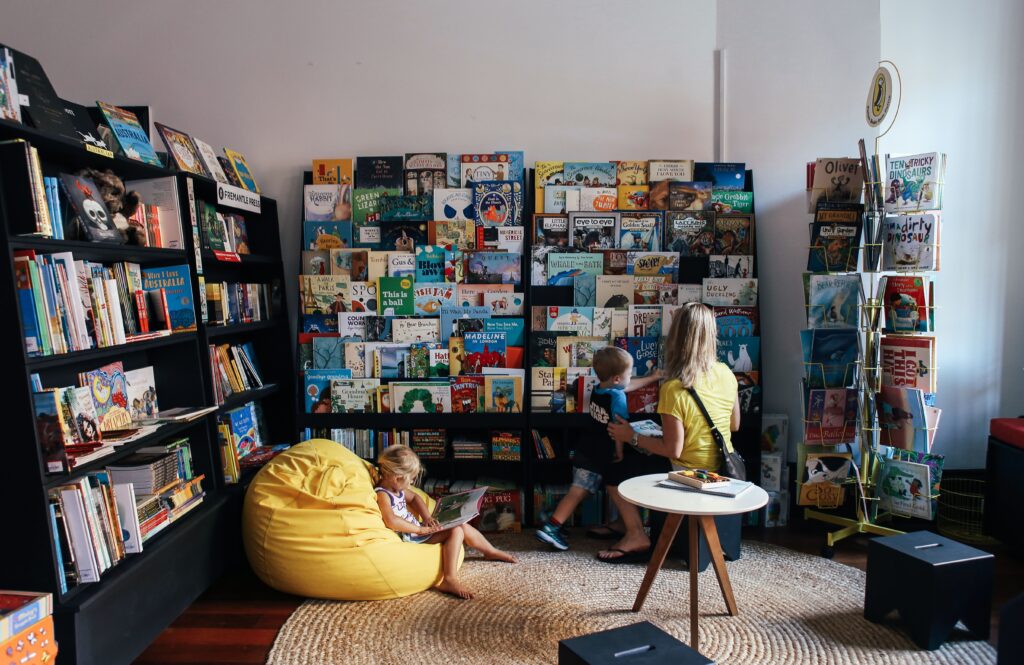A mother and children enjoy reading in a colorful library section with diverse book selections.